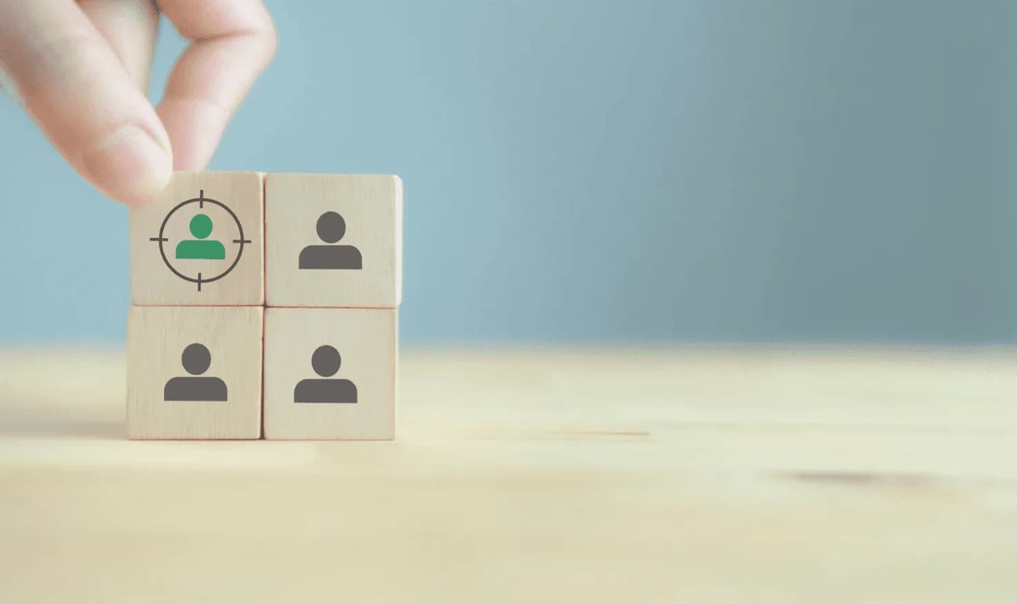 Hand placing wooden block with target symbol over user icons — illustrating precision audience targeting in digital advertising.