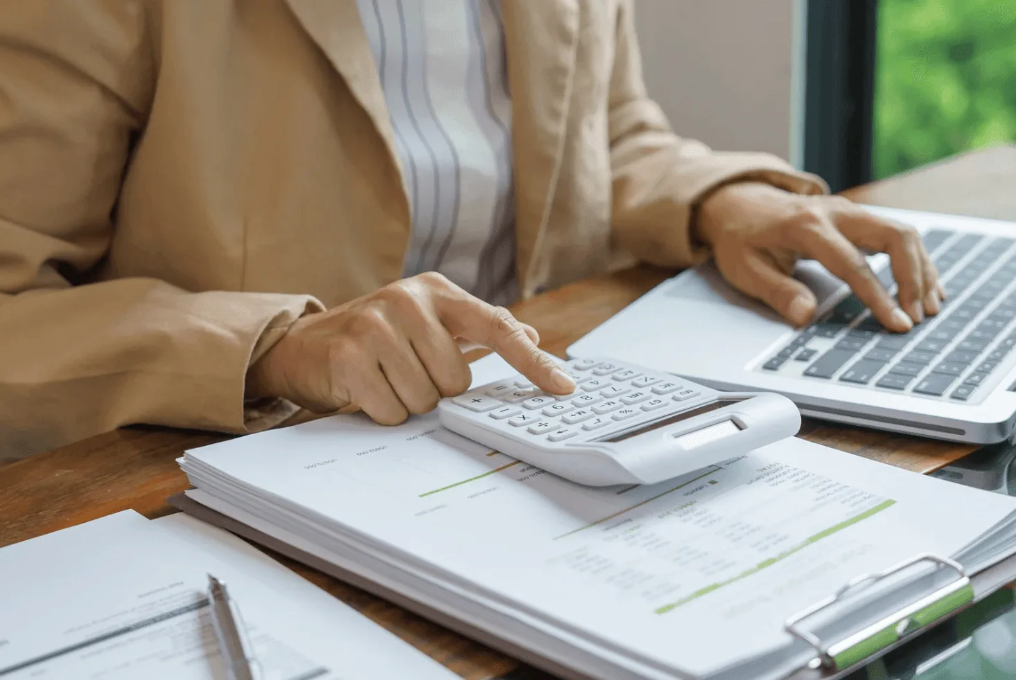 Close-up of hand holding magnifying glass over laptop keyboard — representing scrutiny of agency performance and wasted manual ad management spend.