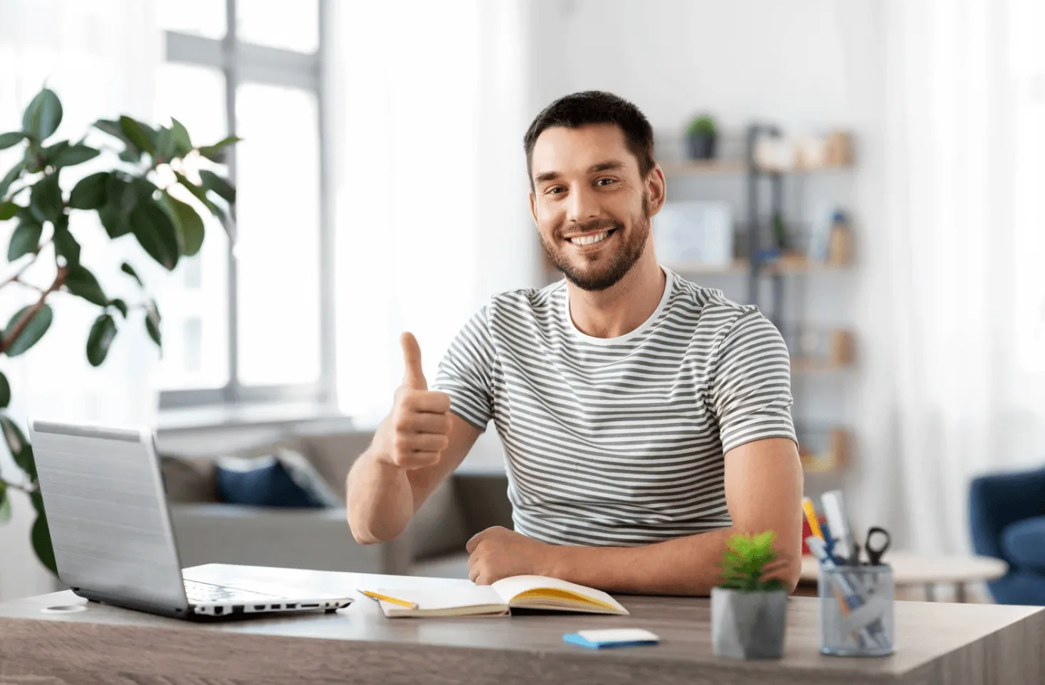 Smiling man at home office giving a thumbs up beside a laptop, reflecting confidence and satisfaction from improved Amazon advertising results.