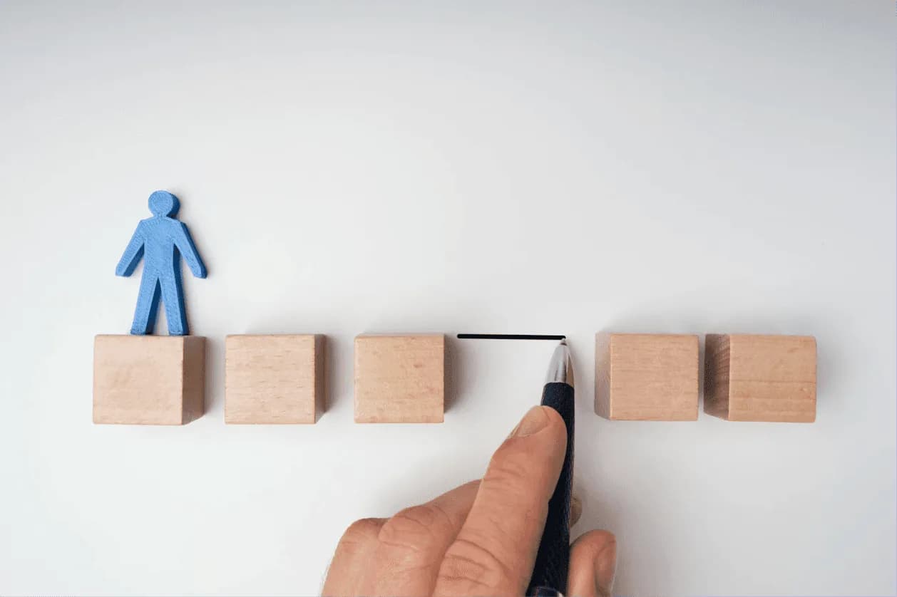 Hand drawing a bridge between wooden blocks with a human figure, representing Autron bridging the gap between full automation and hands-on strategic oversight.