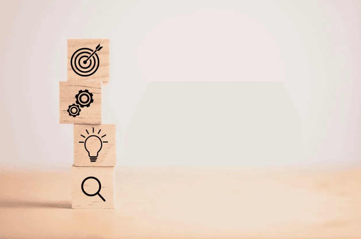 Stacked wooden blocks with icons of target, gears, lightbulb, and magnifying glass, symbolising the risks of automation without clear business objectives and strategic alignment.