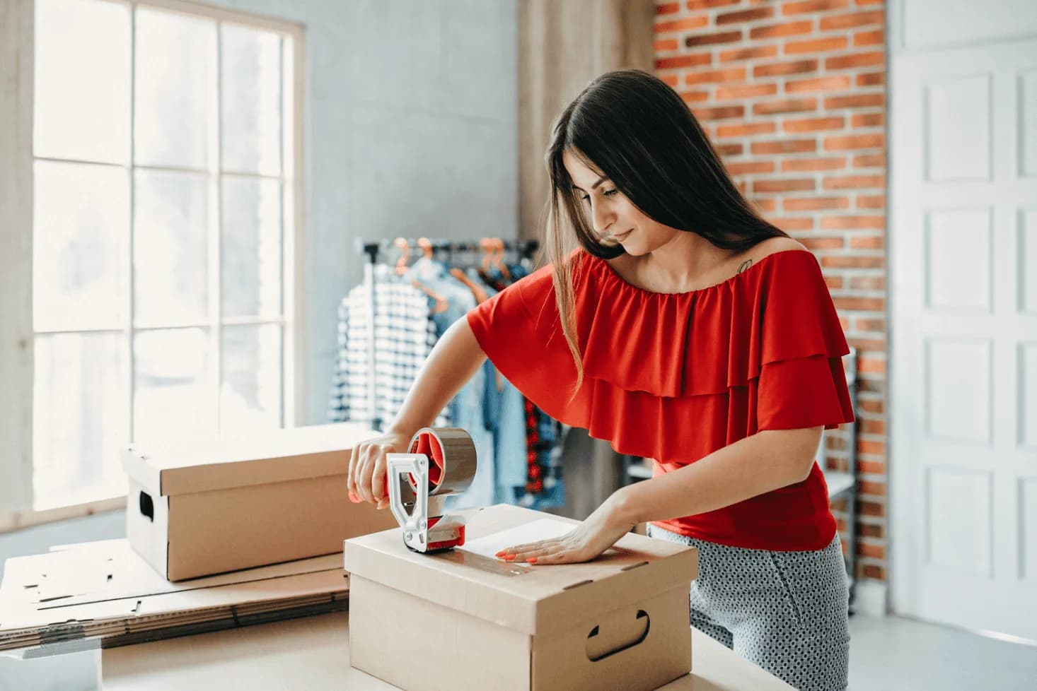Woman sealing a cardboard box with packing tape in a small business setting, illustrating streamlined order fulfillment through automation.