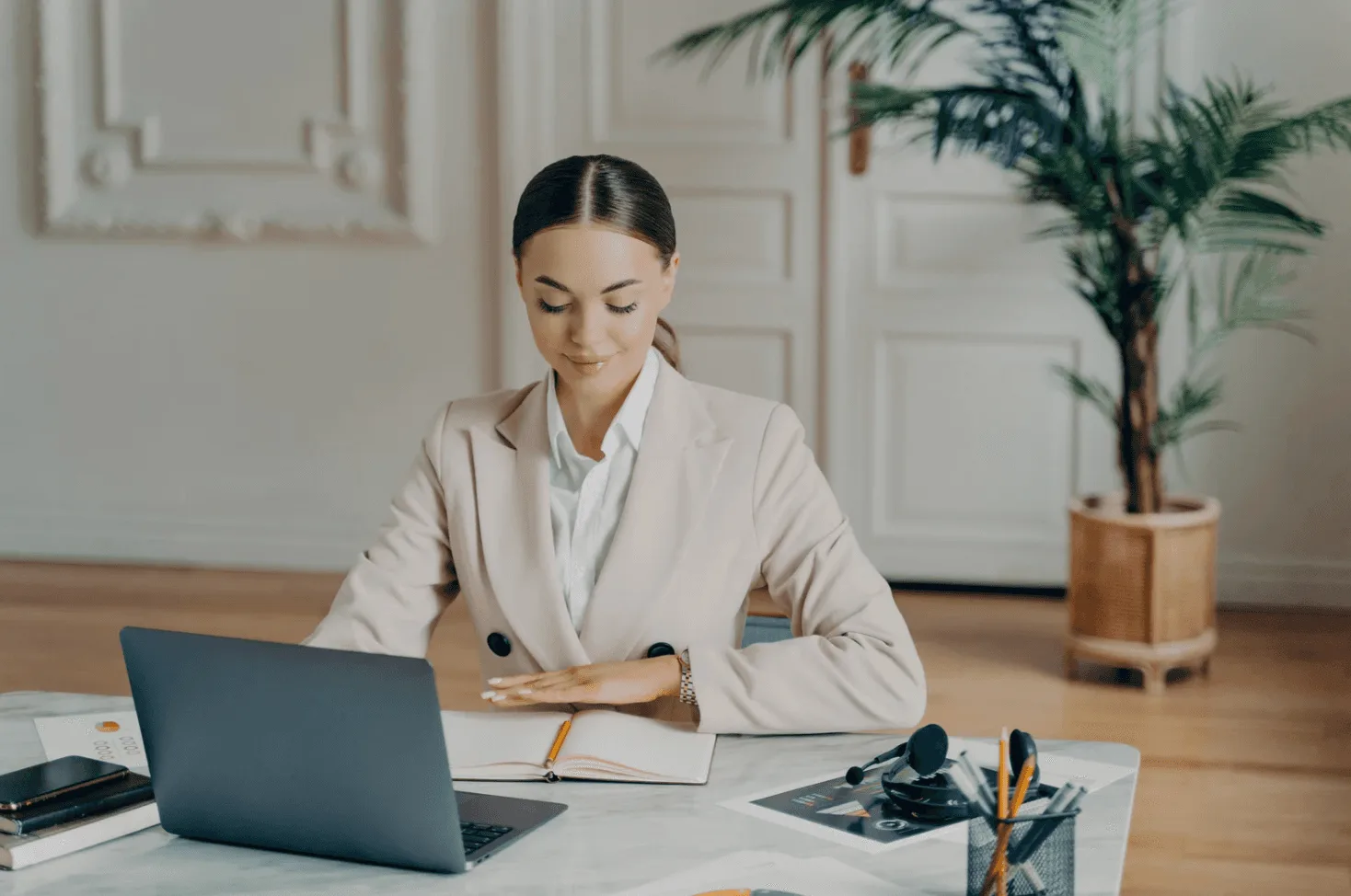 Woman in beige blazer working at desk with laptop and notebook—illustrating smarter ways to scale Amazon ads with less waste.
