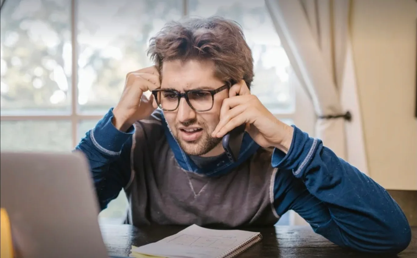 Frustrated Amazon seller on phone with laptop open to campaign metrics – highlighting ad cannibalization challenges and the need for strategic optimisation