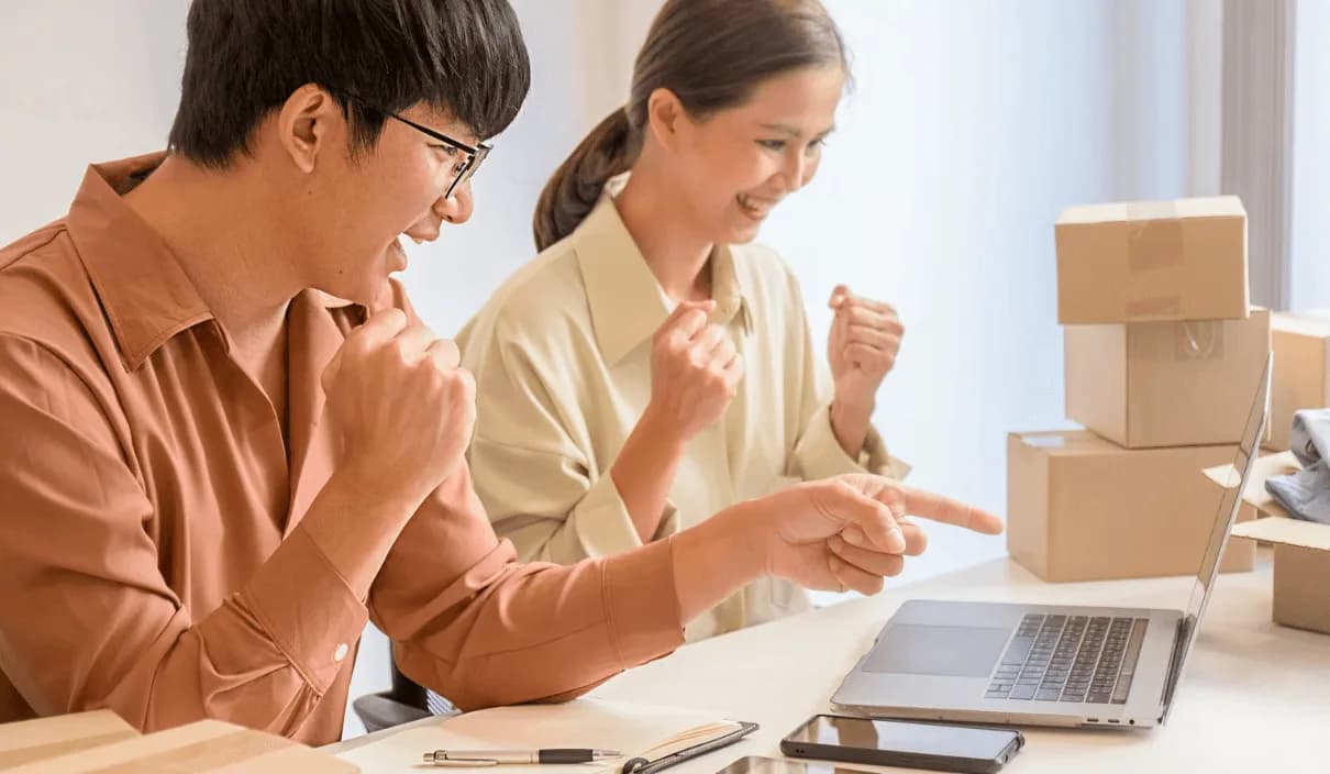Two colleagues cheering over laptop showing improved Amazon rank – demonstrating boosted sales by avoiding PPC ad cannibalization