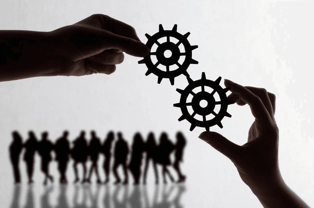 Two hands holding black cogs in sync with a team silhouette in the background – depicting unified Amazon advertising strategy.