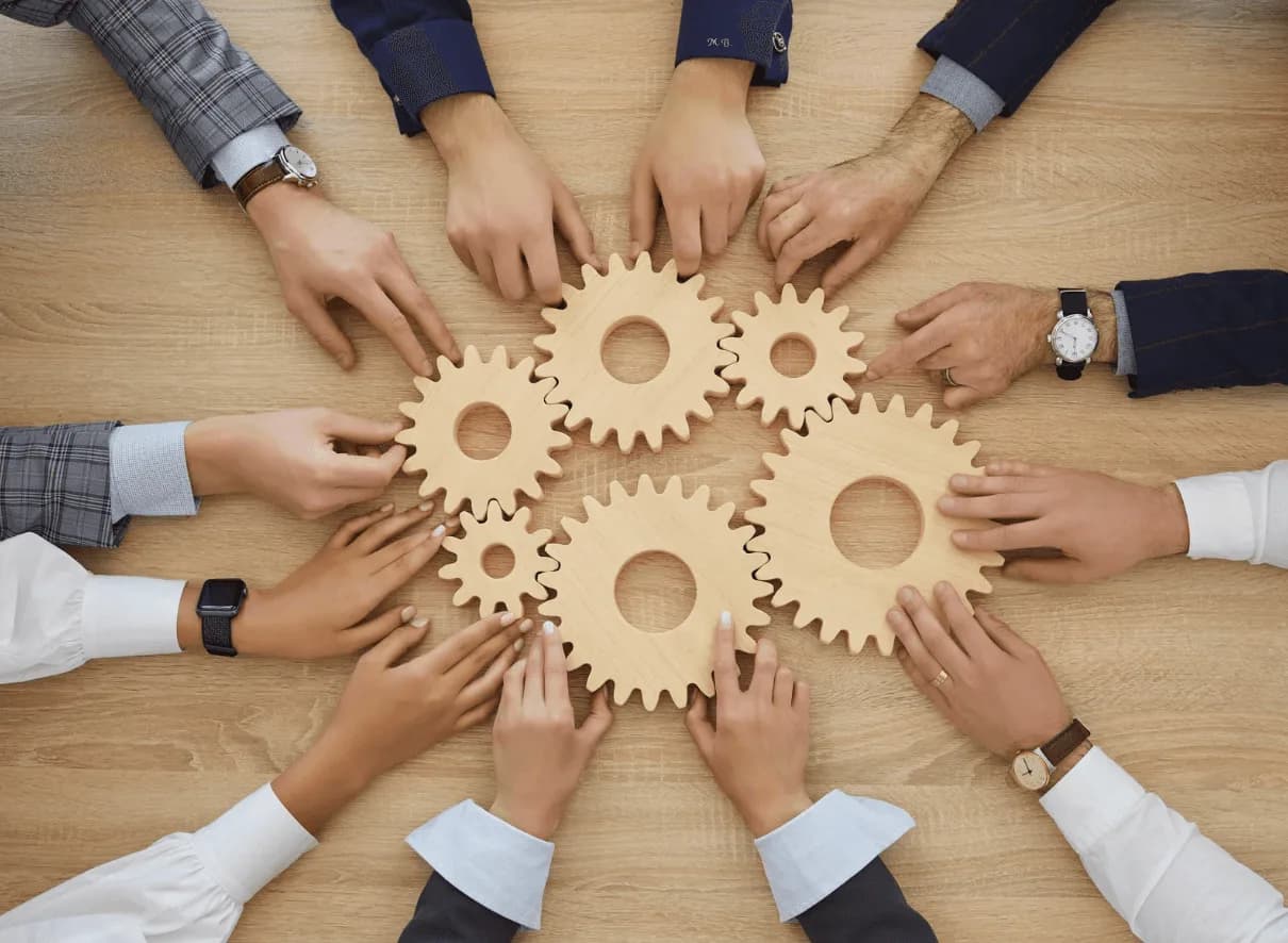 Multiple hands connecting wooden gears on a table – representing synergy and alignment across multiple ASINs in Amazon ad campaigns.
