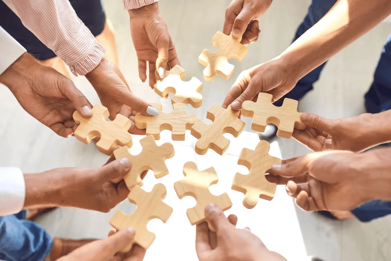 Team of diverse individuals collaborating by connecting wooden puzzle pieces, representing teamwork, integration, and strategic alignment in digital marketing.