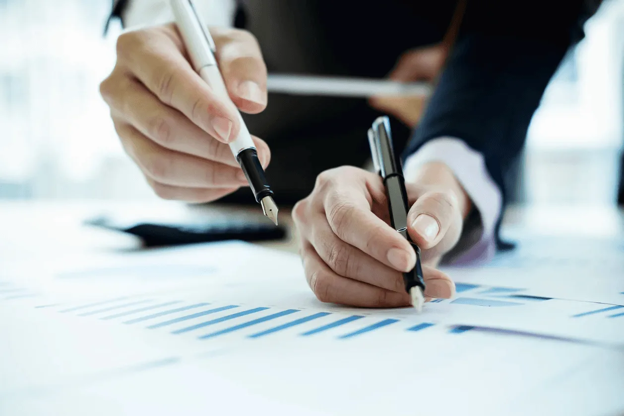 Close-up of professionals reviewing financial charts and graphs with pens, illustrating data-driven decision making in PPC campaign optimisation.
