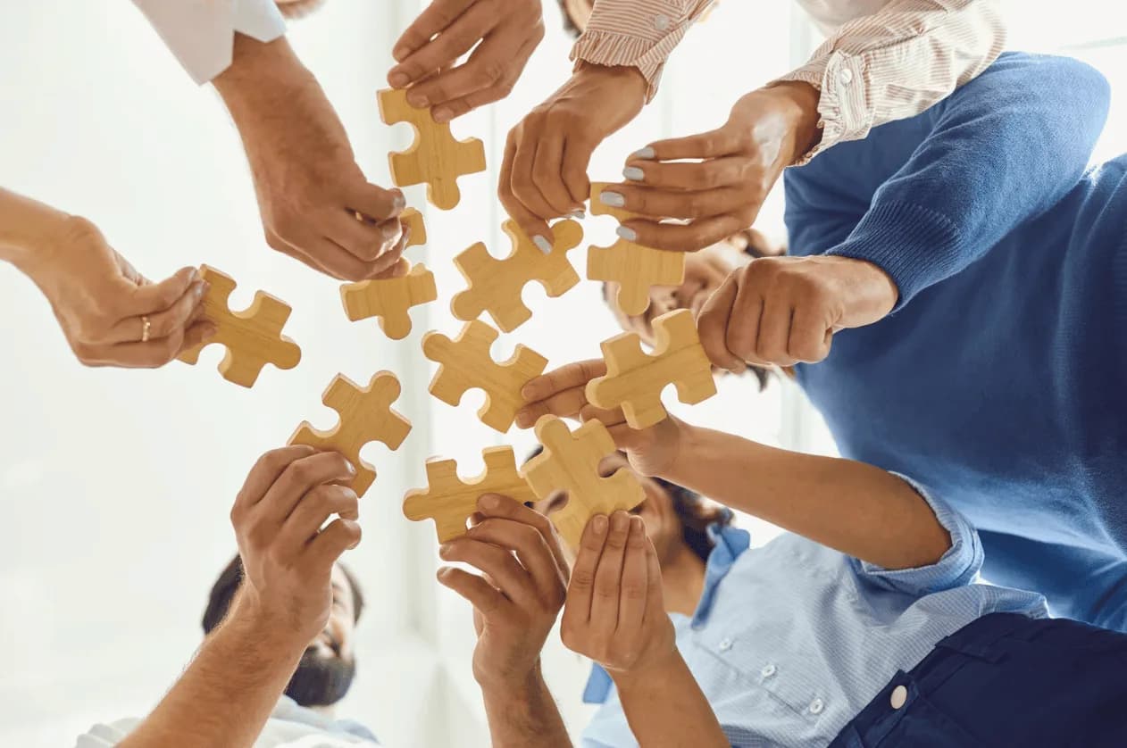 Group of people holding wooden puzzle pieces, representing collaborative strategies to overcome Amazon Advertising challenges.