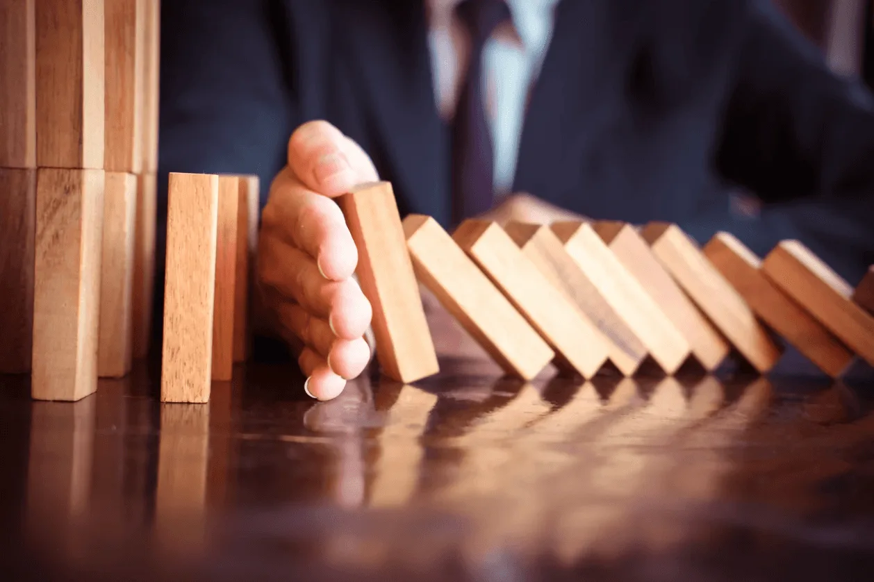 Business professional stopping a chain reaction of falling wooden blocks, symbolising preventing costly mistakes in Amazon Advertising campaigns.