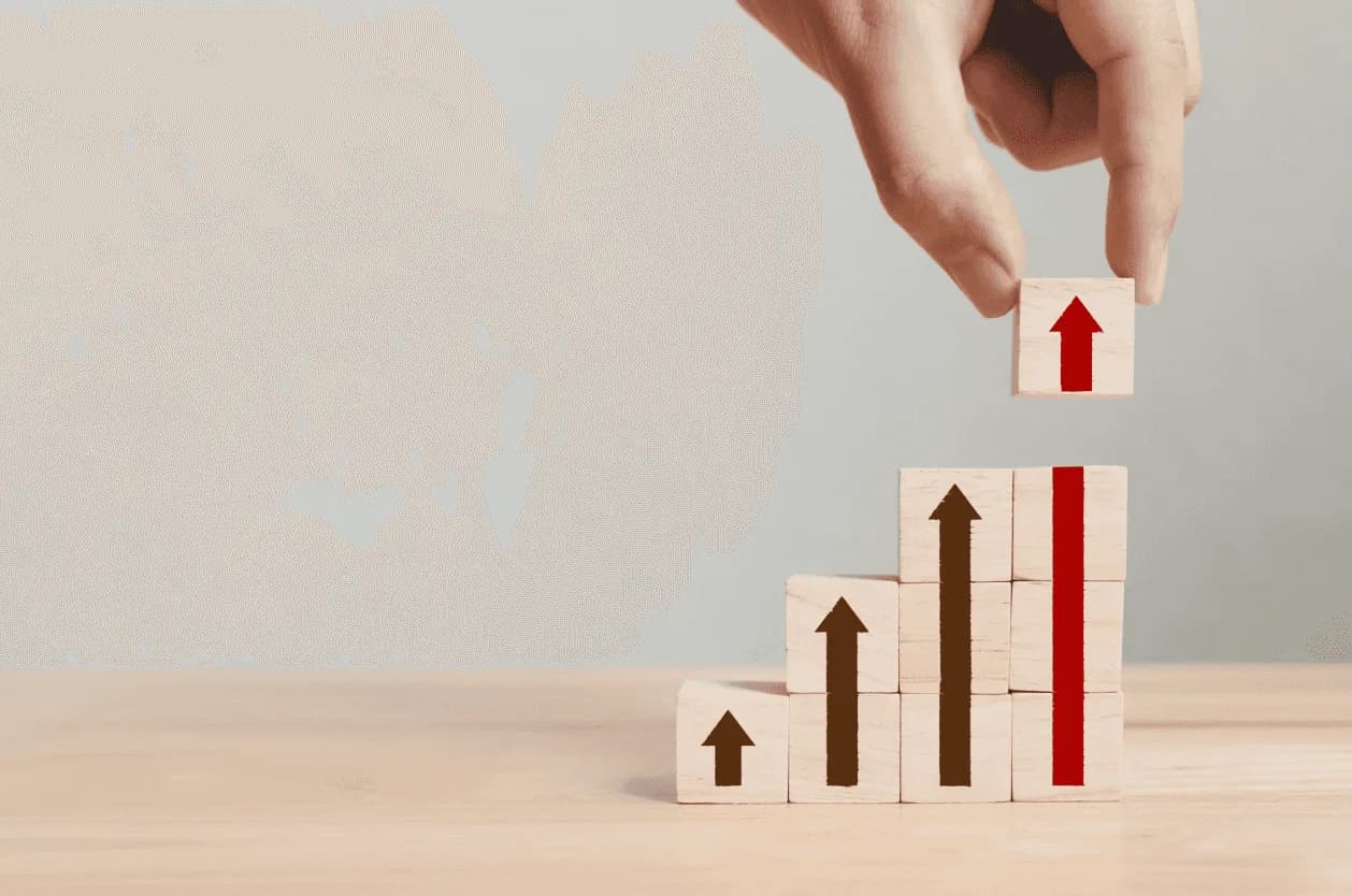 Hand stacking wooden blocks marked with upward arrows, including a highlighted red arrow, depicting Amazon portfolio growth and improved profitability.