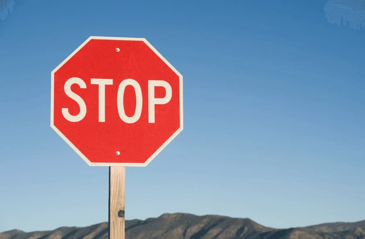 Close-up of a red stop sign against a clear blue sky with distant mountains in the background.