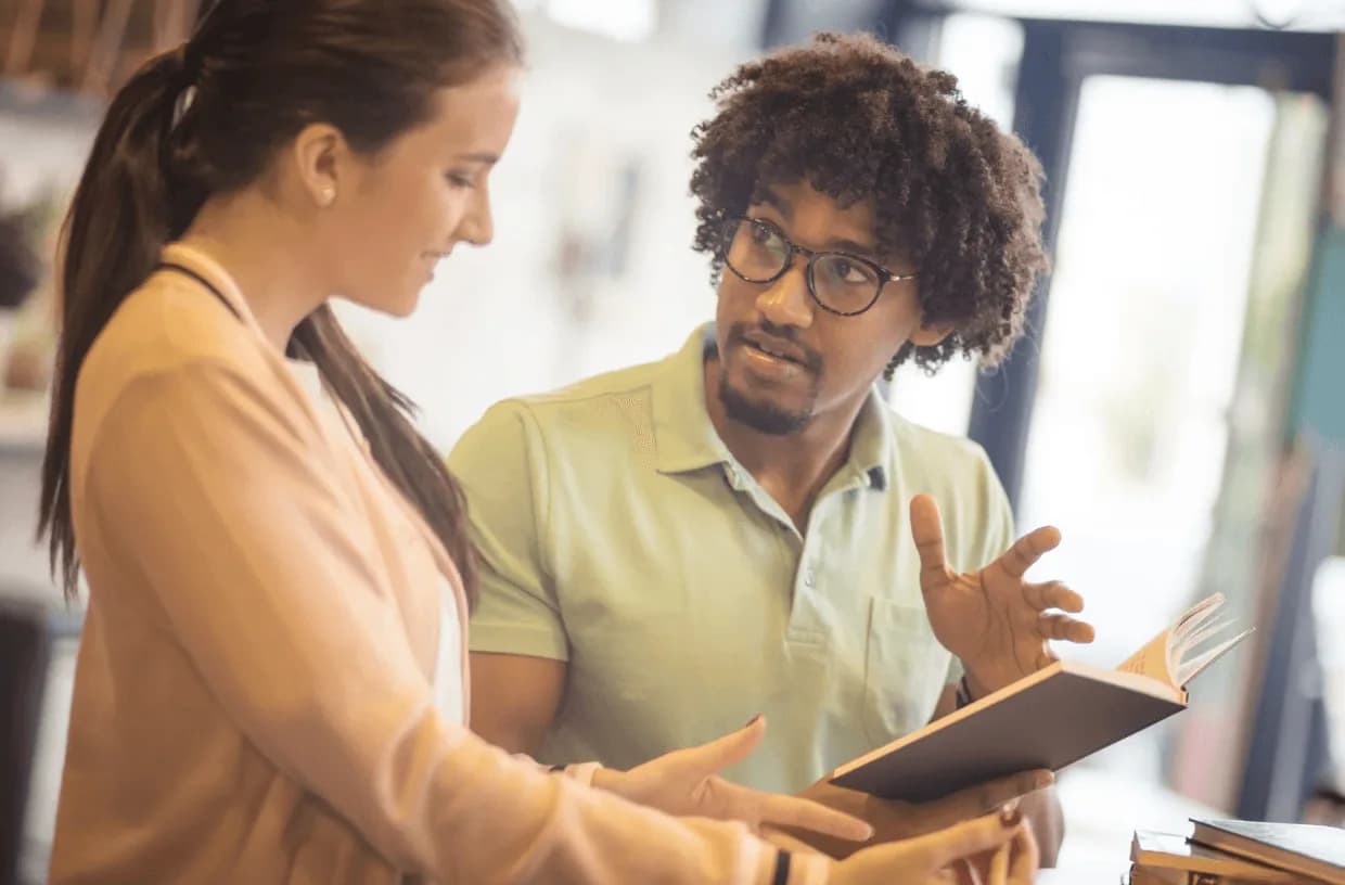 Two colleagues in casual attire discussing ideas over a notebook in a creative workspace
