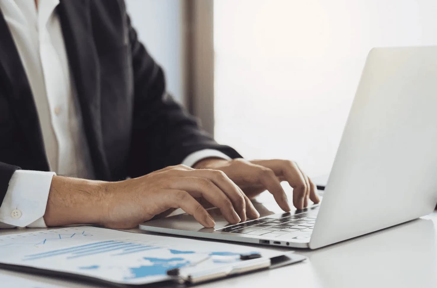 Business professional typing on a laptop next to performance reports, illustrating real-time Amazon FBA budget reallocation during peak sales windows.