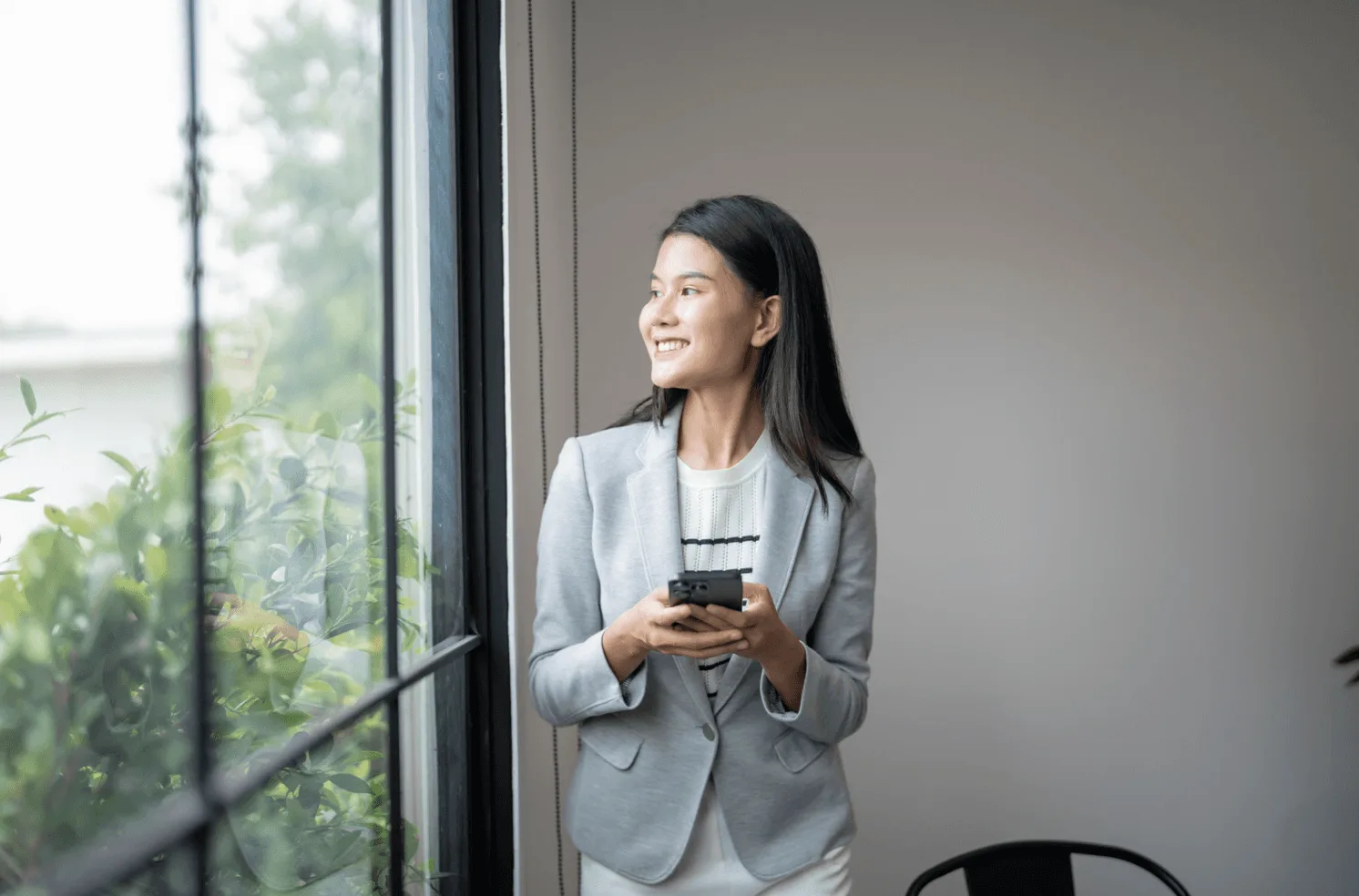 Business professional using a smartphone near a window, representing automation tools and real-time decision making in Amazon advertising.