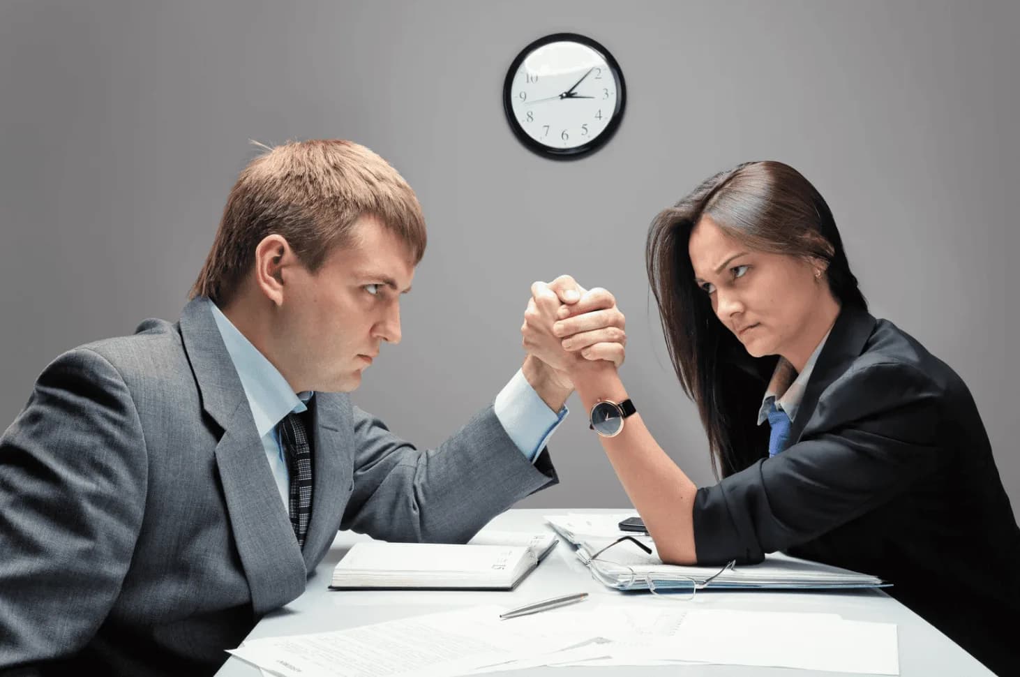 Man and woman arm-wrestling across a desk, symbolising internal competition between Amazon ad campaigns when SP, SB, and SD fight for the same traffic.