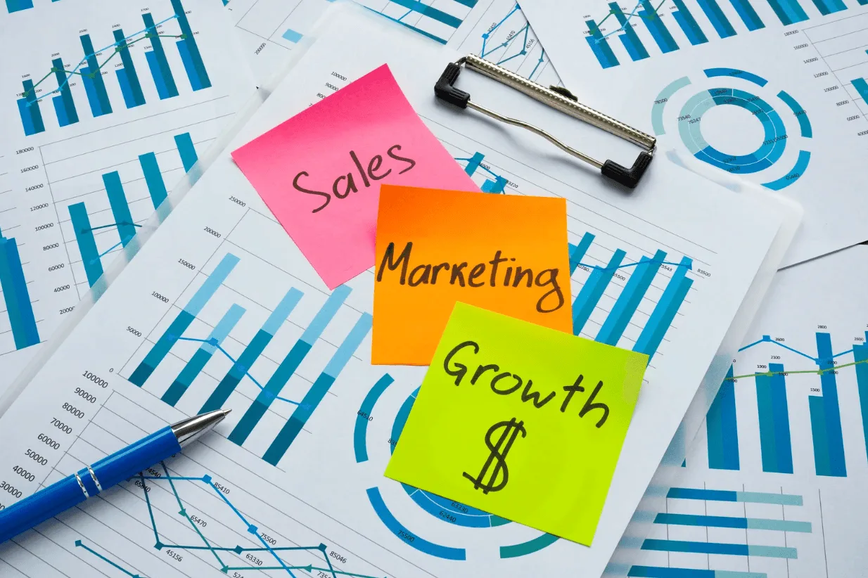 Sticky notes labelled Sales, Marketing, Growth on financial reports with charts, illustrating strategy alignment for sustainable ad success