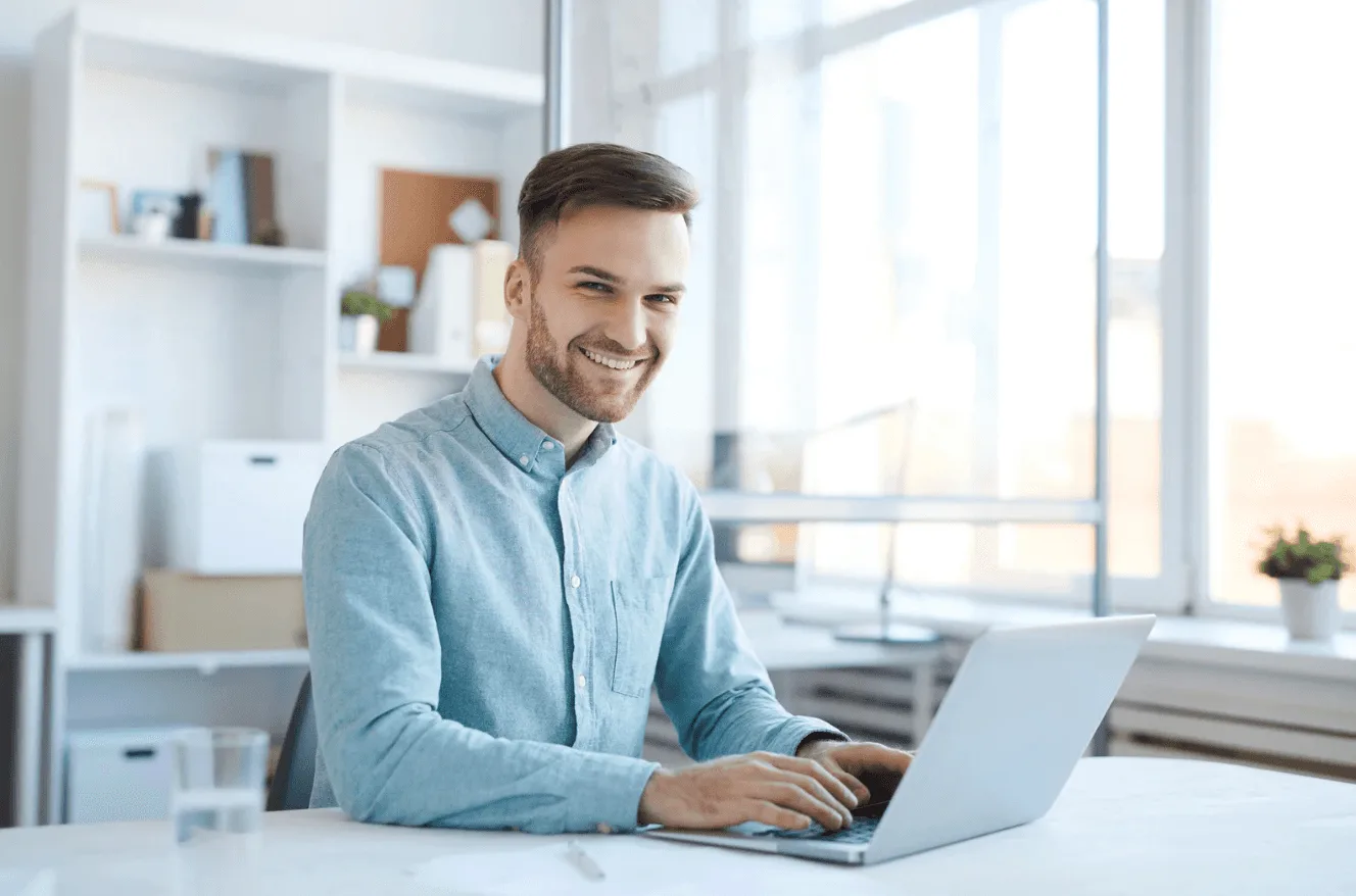 Young professional smiling while using a laptop, illustrating the power of authentic user-generated content in Amazon Ads.